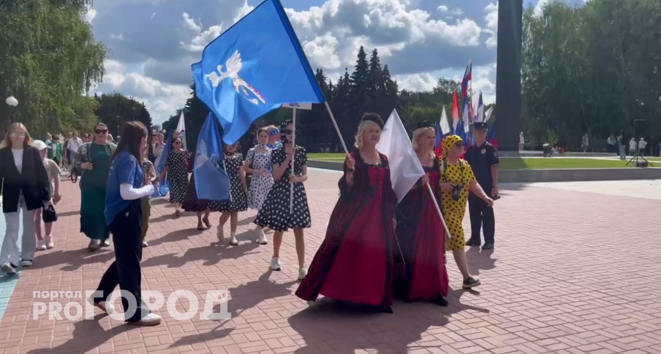 Люди в костюмах с флагами идут через Йошкар-Олу в честь Дня города